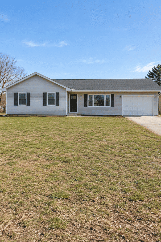 Ranch house with plain vinyl siding and bare lawn before exterior and landscape update
